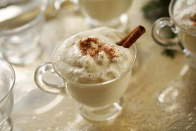 Egg nog on a silver tray in a glass punch cup with cinnamon stick stirrer