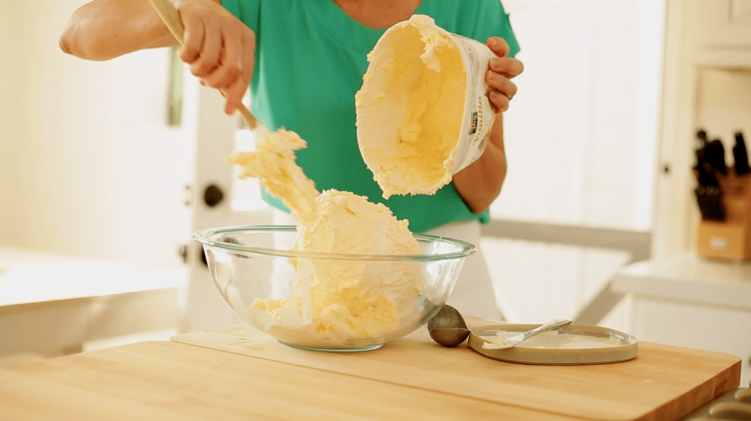 a Person transferring softened vanilla ice cream from a carton into a bowl