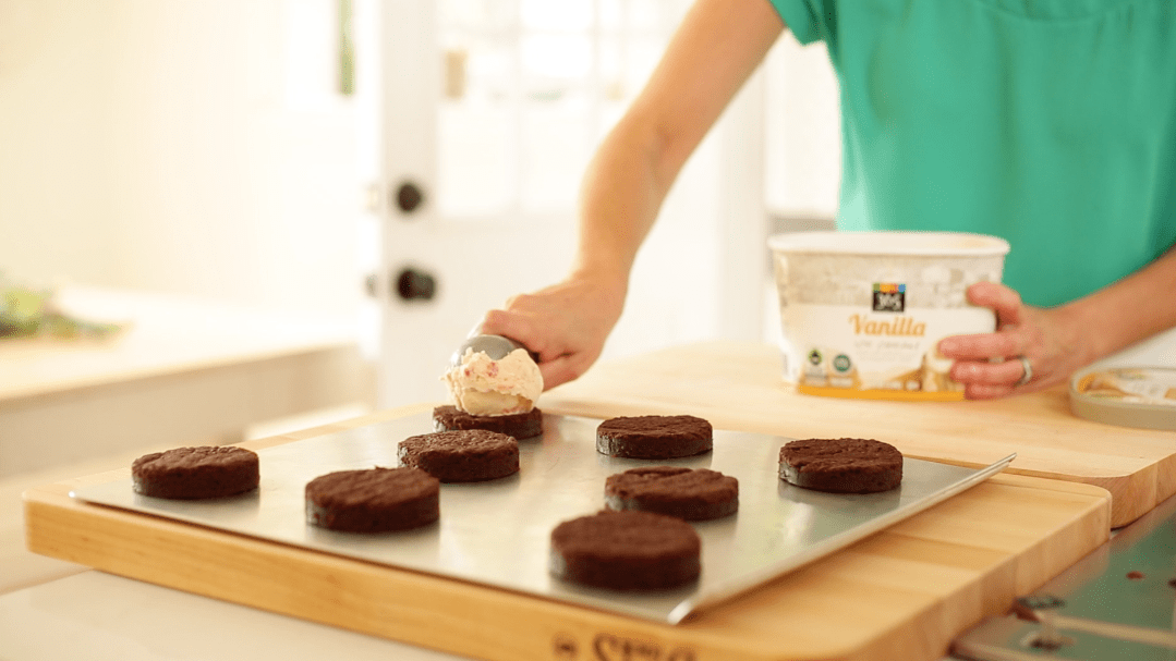 a Person adding a scoop of candy cane ice cream to brownie bases on a sheet pan