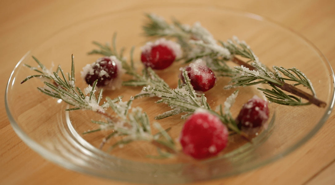 Fresh rosemary and cranberry garnishes covered in sugar on a clear plate