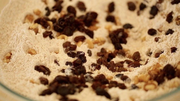 Adding raisins and walnuts to flour in a large glass bowl