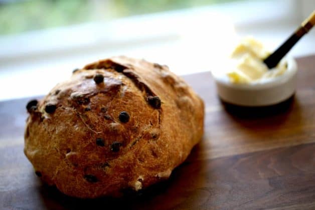 No-Knead Cinnamon Raisin Bread resting on a cutting board with a dish of butter