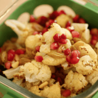 A close up of a plastic container filled with Cauliflower, pomegranate seeds, and golden raisins