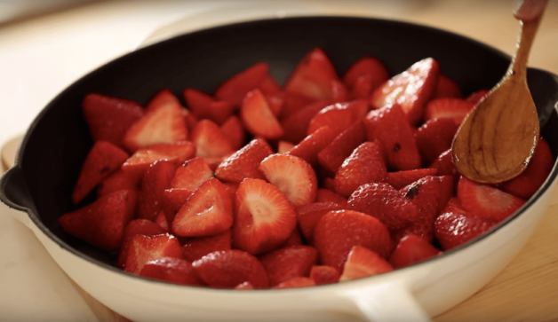 strawberry mixture in a skillet being leveled with a wooden spoon