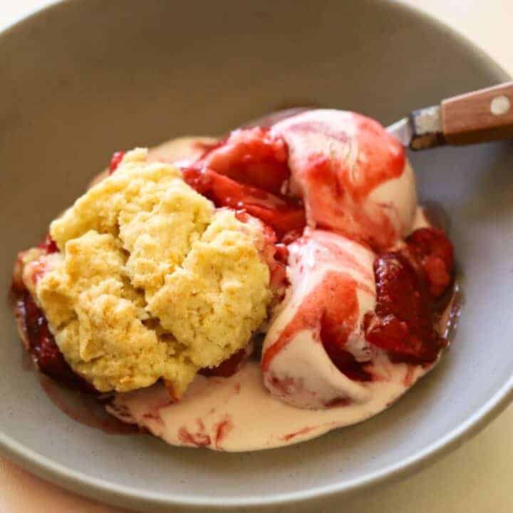 a bowl of ice cream with cobbler biscuits and syrupy strawberries