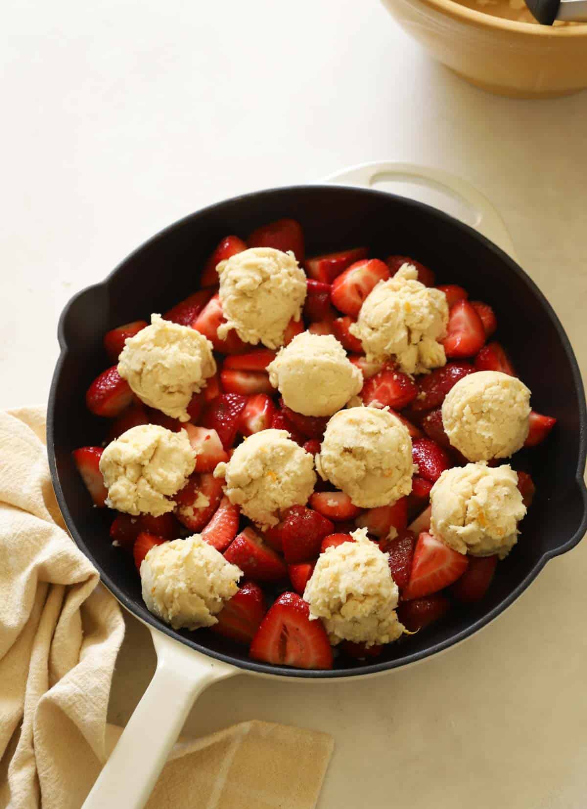 a strawberry cobbler ready for the oven topped with biscuits