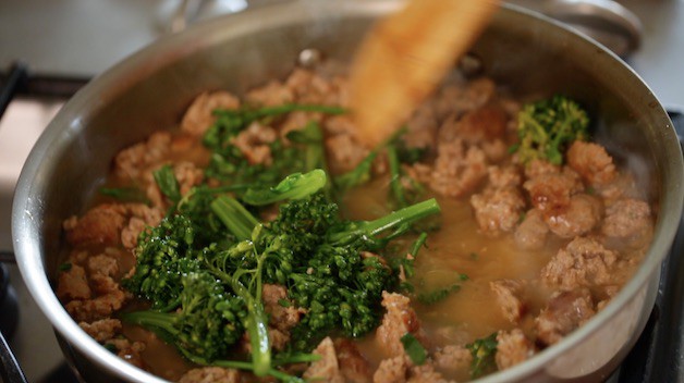 Tossing cooked baby broccoli with Sweet Italian Sausage