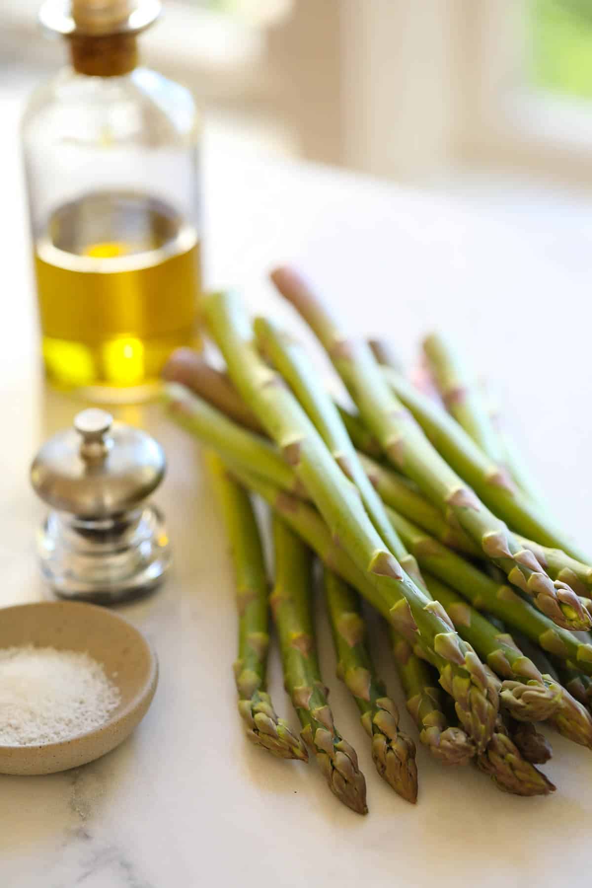 A bunch of fresh asparagus on the counter with Olove Oil Salt and Pepper