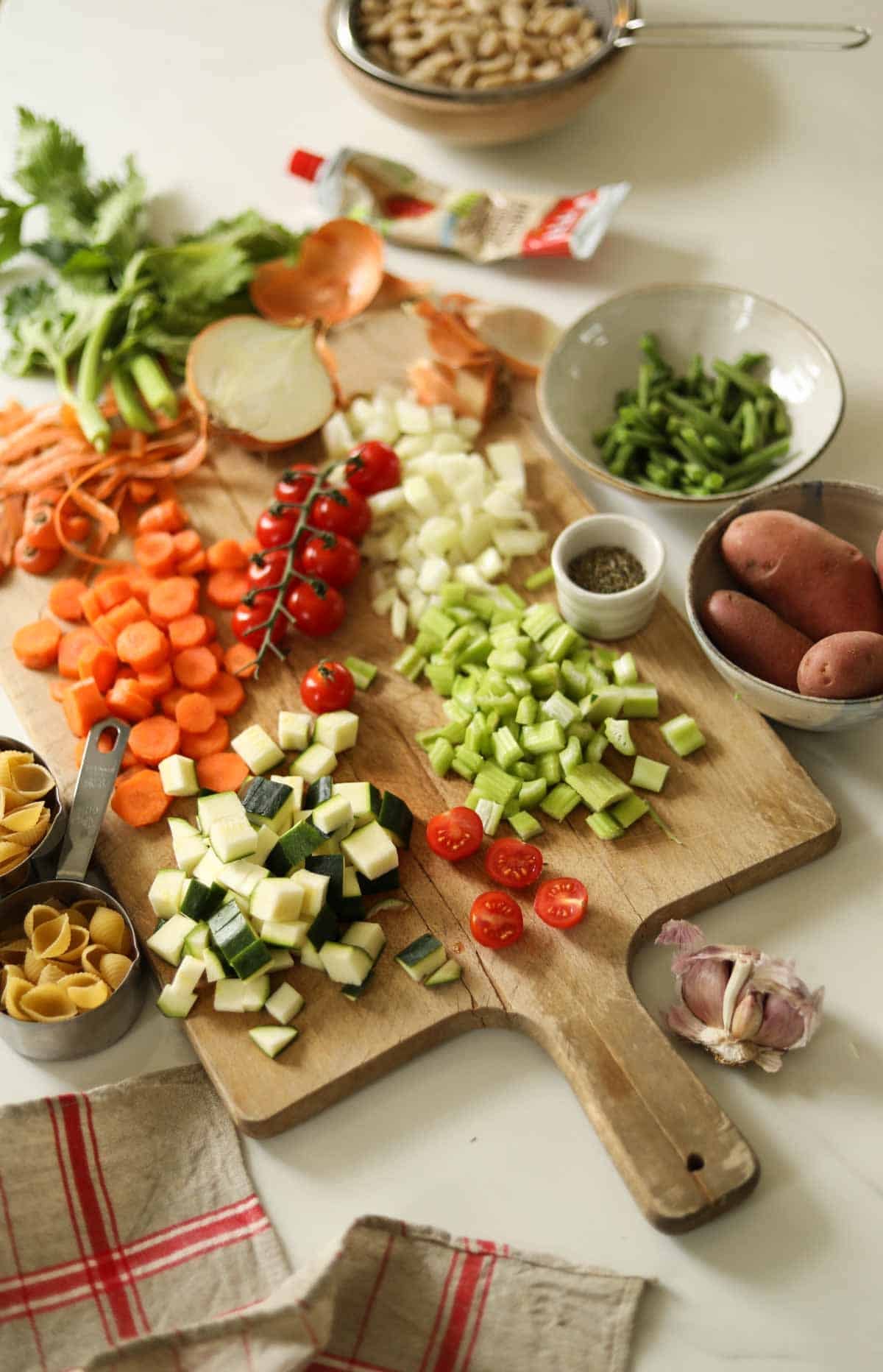 Chopped vegetables on a cutting board with ingredients for soup laid on a counter.
