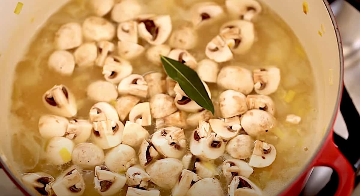 white button mushrooms and bay leaf floating in a chicken pot pie soup