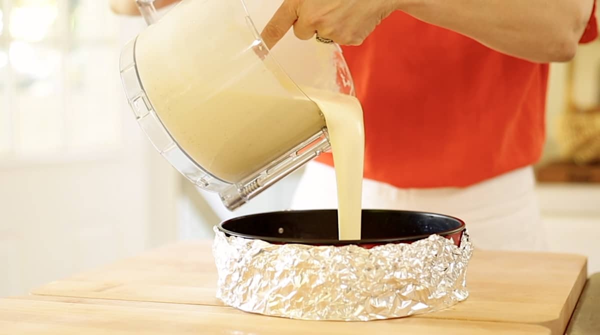 a person pouring the cheesecake filling into a cheesecake pan