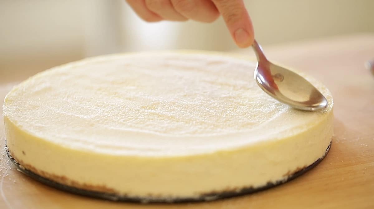 a person smoothing out a layer of sugar on top of cheesecake