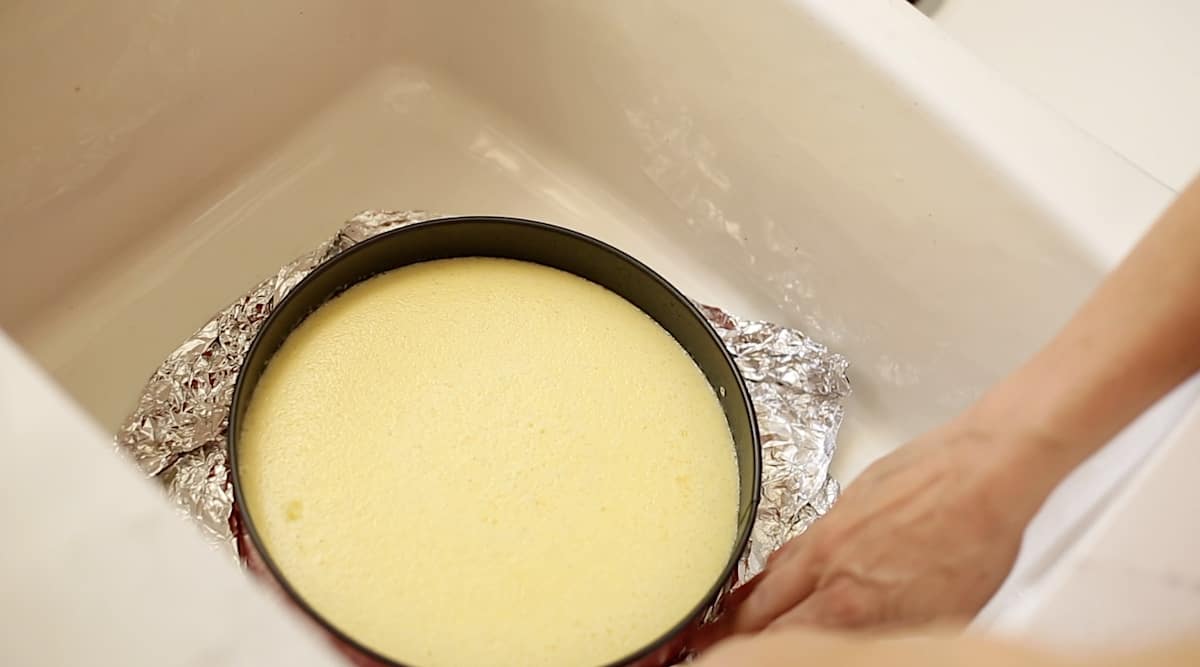 a cheesecake in the sink with a person removing the foil