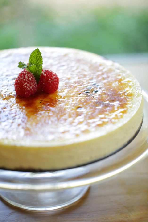 Creme Brulee Cheesecake on a cake stand with a raspberry and mint garnish