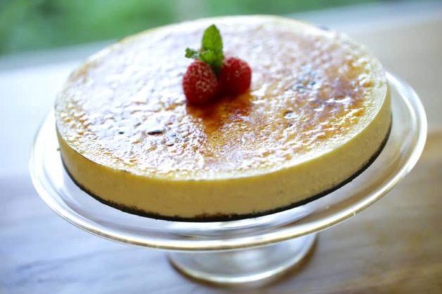 Creme Brulee Cheesecake Recipe on a cake stand with raspberry and mint garnish