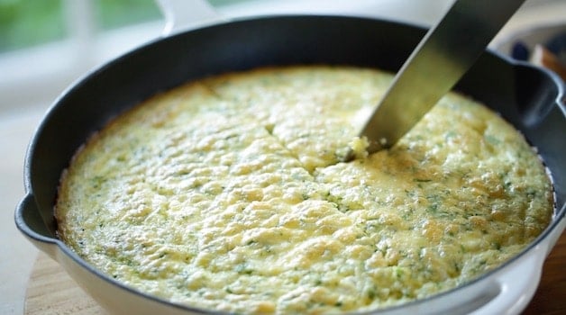 Slicing an egg casserole in a white skillet with a large Chef Knife