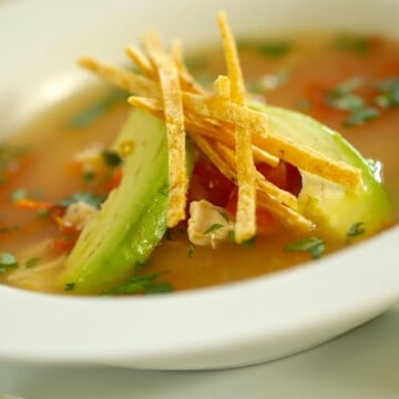 Easy Tortilla Soup Recipe in a white bowl garnished with Tortillas and Avocados