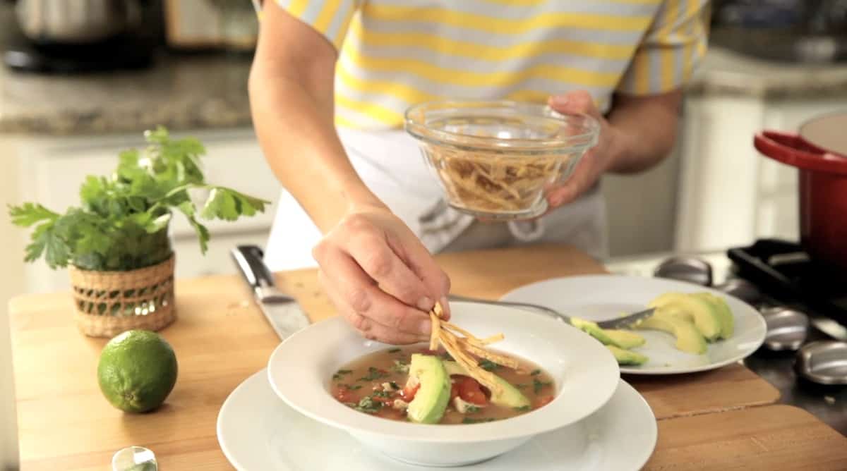 a person placing tortilla strips on top of a soup