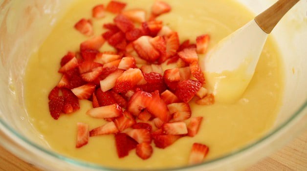 Adding diced strawberries to a bowl of muffin batter