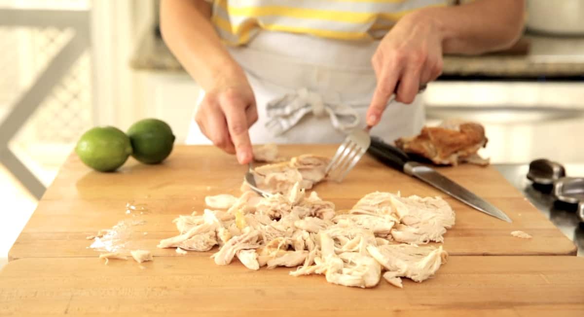 a person shredding chicken on a cutting board