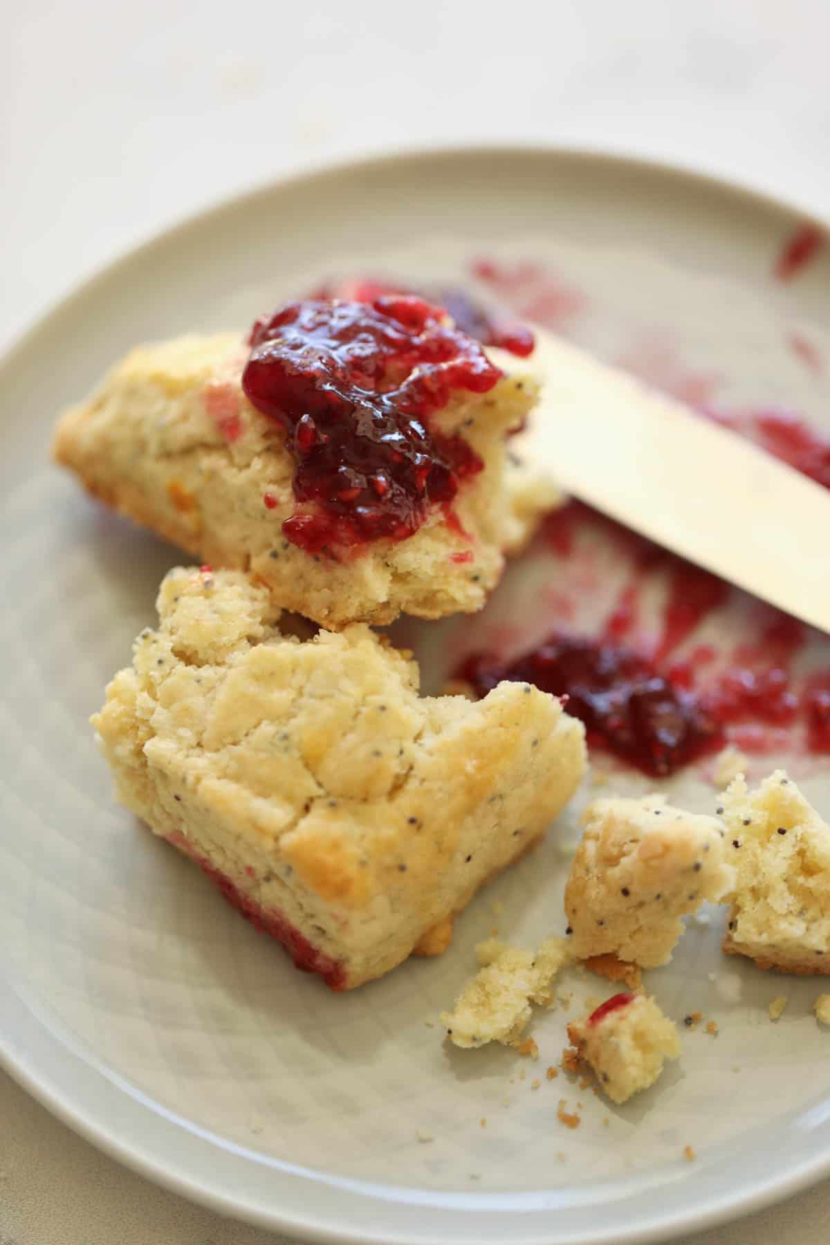 a lemon poppy seed scone broken in half on a plate topped with raspberry jam