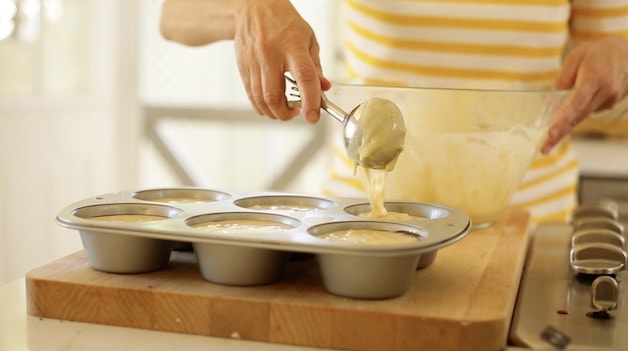 scooping banana muffin batter into a jumbo muffin tin