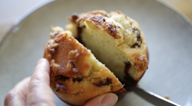 slicing open a banana nut muffin with black bottoms