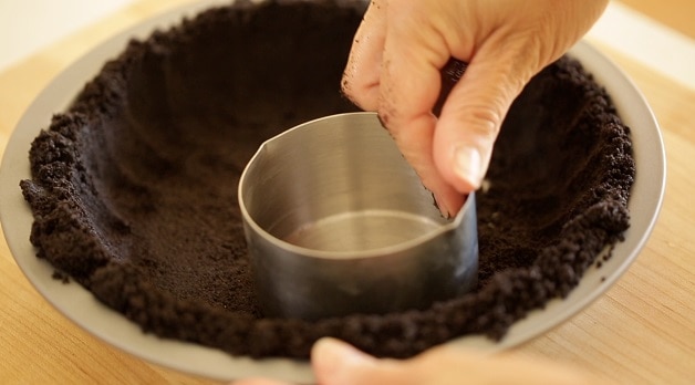 Pressing pie crumbs into pie tin with measuring cup