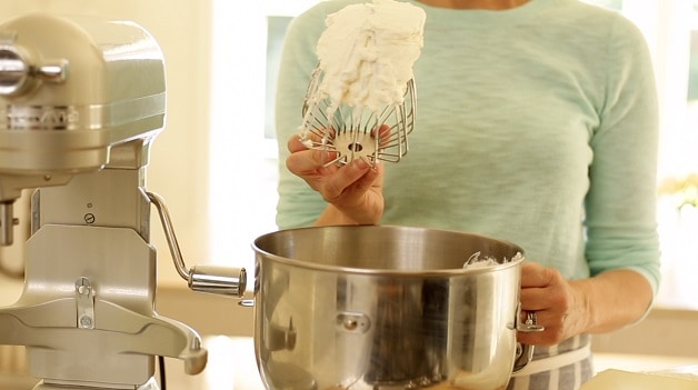 a person holding up a whisk attachment and showing the stiffness of whipped cream