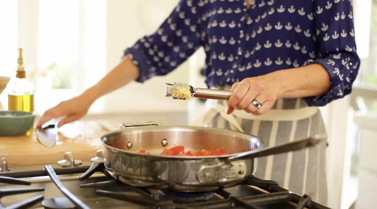 a person adding garlic to a homemade tomato sauce in a pan
