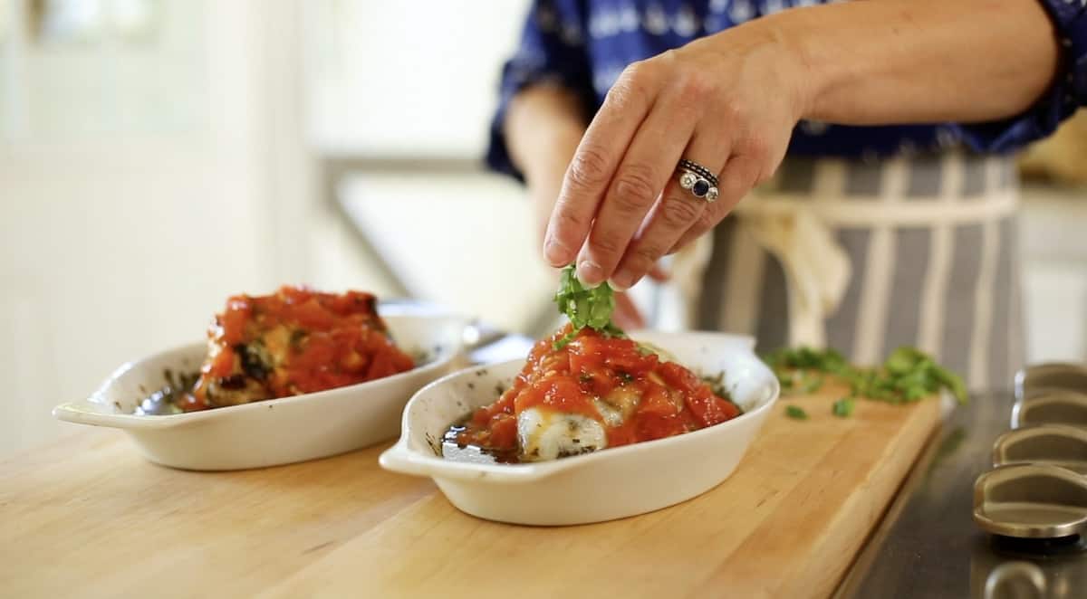 a person adding basil to the top of a pesto chicken bake