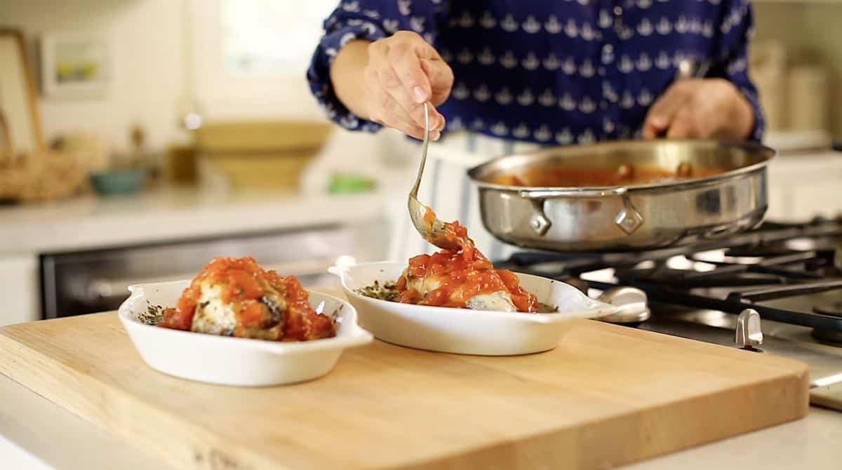 a person ladeling tomato sauce onto 2 chicken bakes