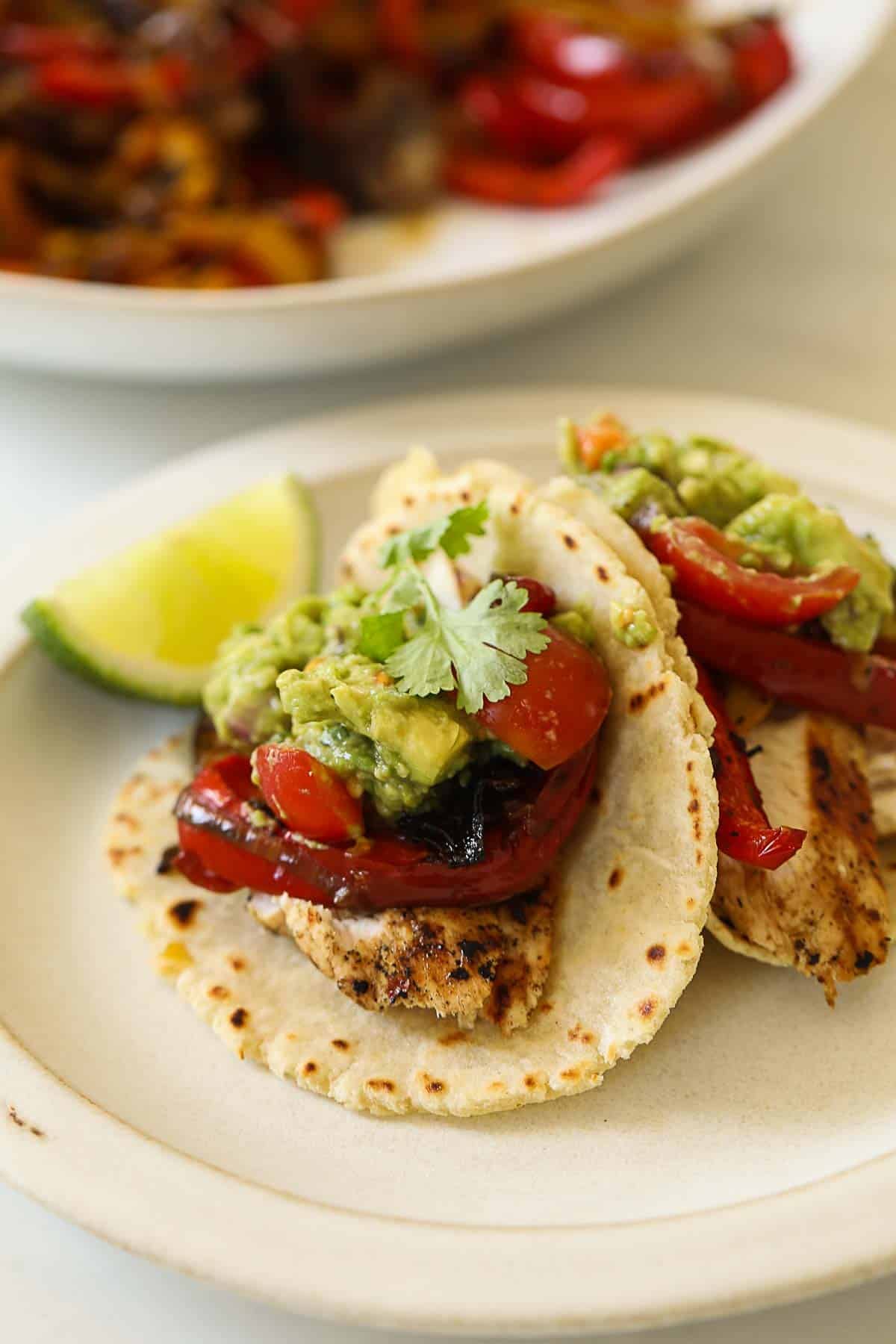 a plate with two chicken fajita tacos and guacamole.