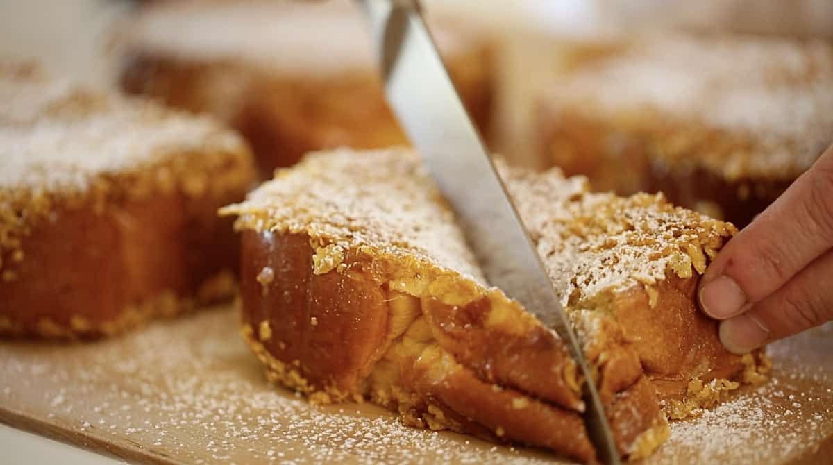 a person slicing a thick piece of French toast on the diagonal with a chef's knife