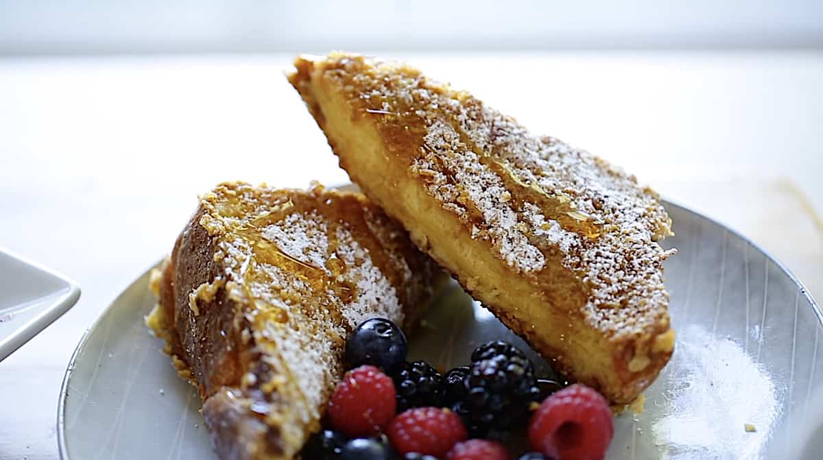 Two slices of French toast on a plate with berries and maple syrup