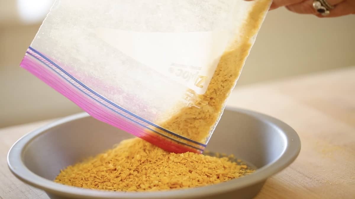 crushed corn flakes being poured from a plastic bag to a metal pie plate