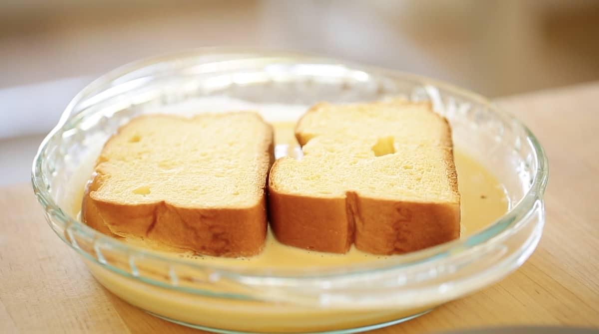 Thick slices of brioche bread soaking in egg custard in a pie plate