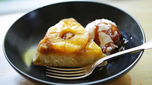 A slice of Pineapple Upside Down Cake in a black bowl with ice cream