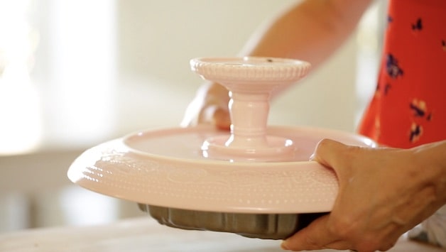 Flipping a pineapple upside cake onto a pink cake stand