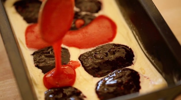 dollops of fruit puree being adding to vanilla ice cream in a loaf pan 