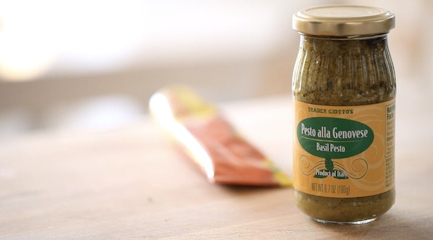 a fjar of pesto on a cutting board with a tube of tomato paste in the background