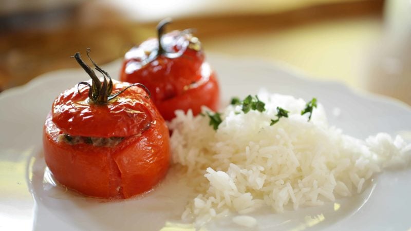 Due pomodori ripieni su un piatto bianco con riso e prezzemolo