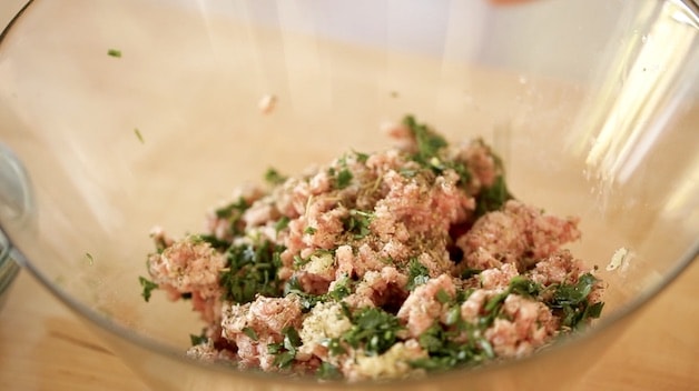 Ground Pork in a clear bowl with herbs and seasonings