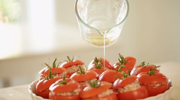 adding white wine to a baking dish of stuffed tomtatoes