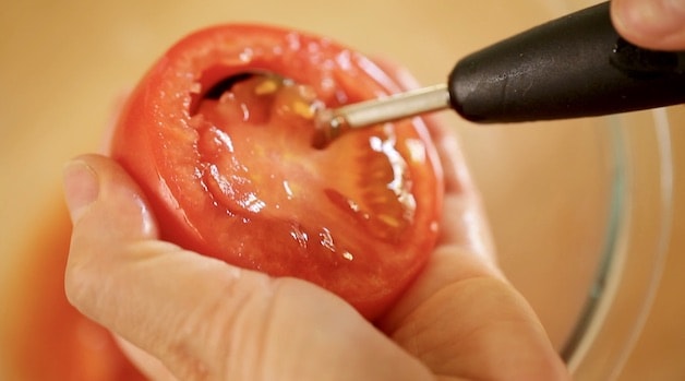 A tomato Cut in half with a melon baller removing the flesh