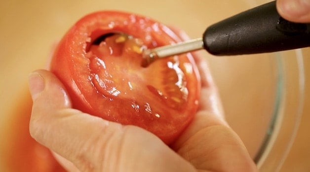 Une tomate coupée en deux avec une cuillère parisienne en retirant la chair