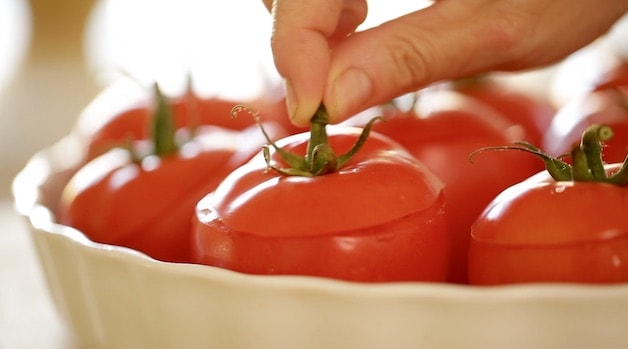 Fingertips holding the top of a tomato top