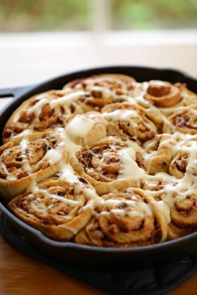 cream cheese glaze drizzled on top of overnight cinnamon rolls in a cast iron skillet