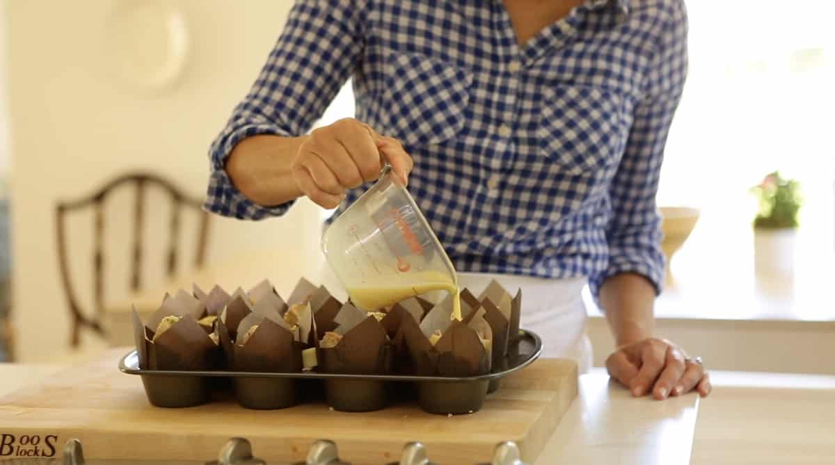 A person standing in front of a table pouring egg custard into a muffin tin