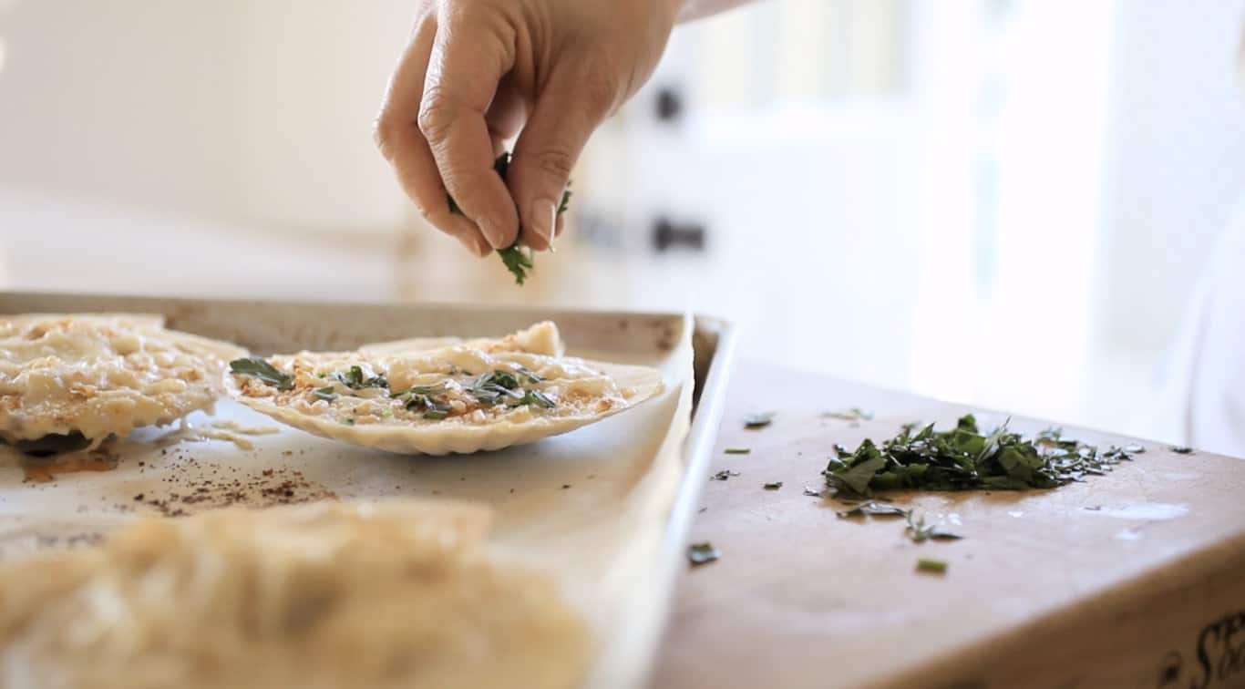 placing parsley on scallop shells on a baking sheet